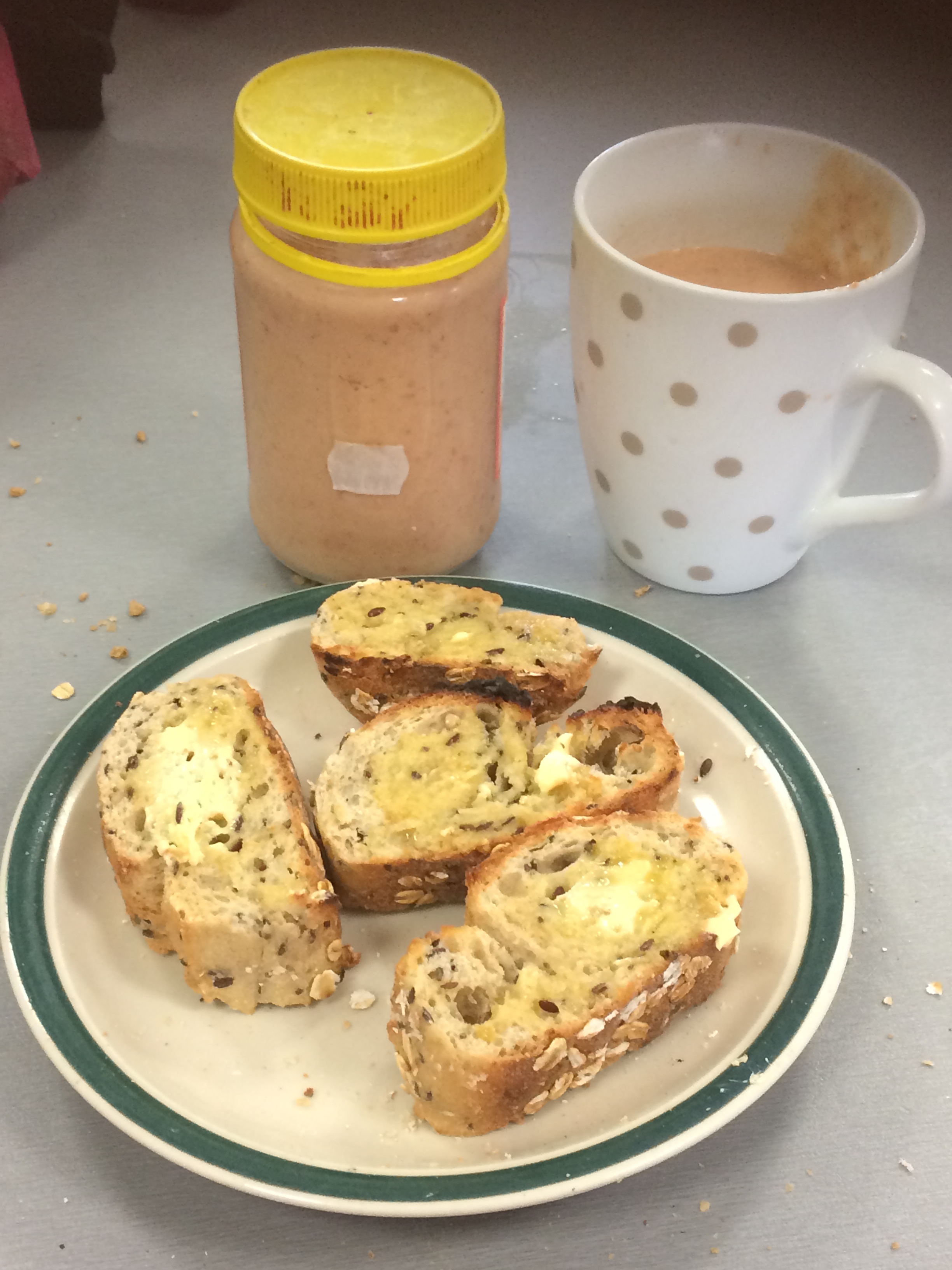 Four small slices of margarined wholegrain toast on a plate. Behind them is a glass jar full of smoothie (smoothie is light pink, jar lid is yellow) and a mug (white with brown polka dots) full of the same.