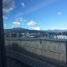 Powerlines, a wall, railway tracks and passing houses viewed from the train - mountains in the distance