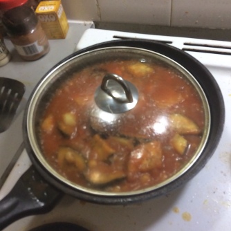 Eggplant, carrot and chickpeas simmering in a rich tomatoey sauce in a black deep frypan with clear lid on