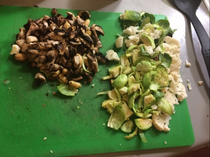on a green chopping board are two piles - one is of mushrooms and peanuts, the other is Brussels sprouts and cauliflower