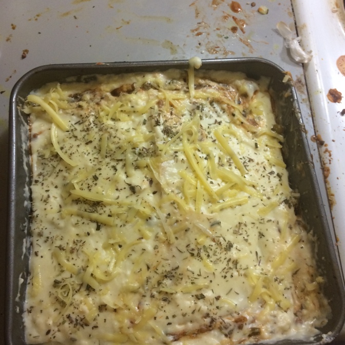 Assembled lasagna in the baking dish with grated cheese and mixed herbs scattered on top