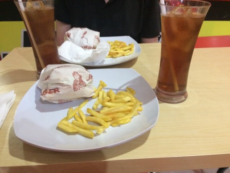 Two glasses of iced tea, two burgers wrapped in paper and a side of yellow fries.