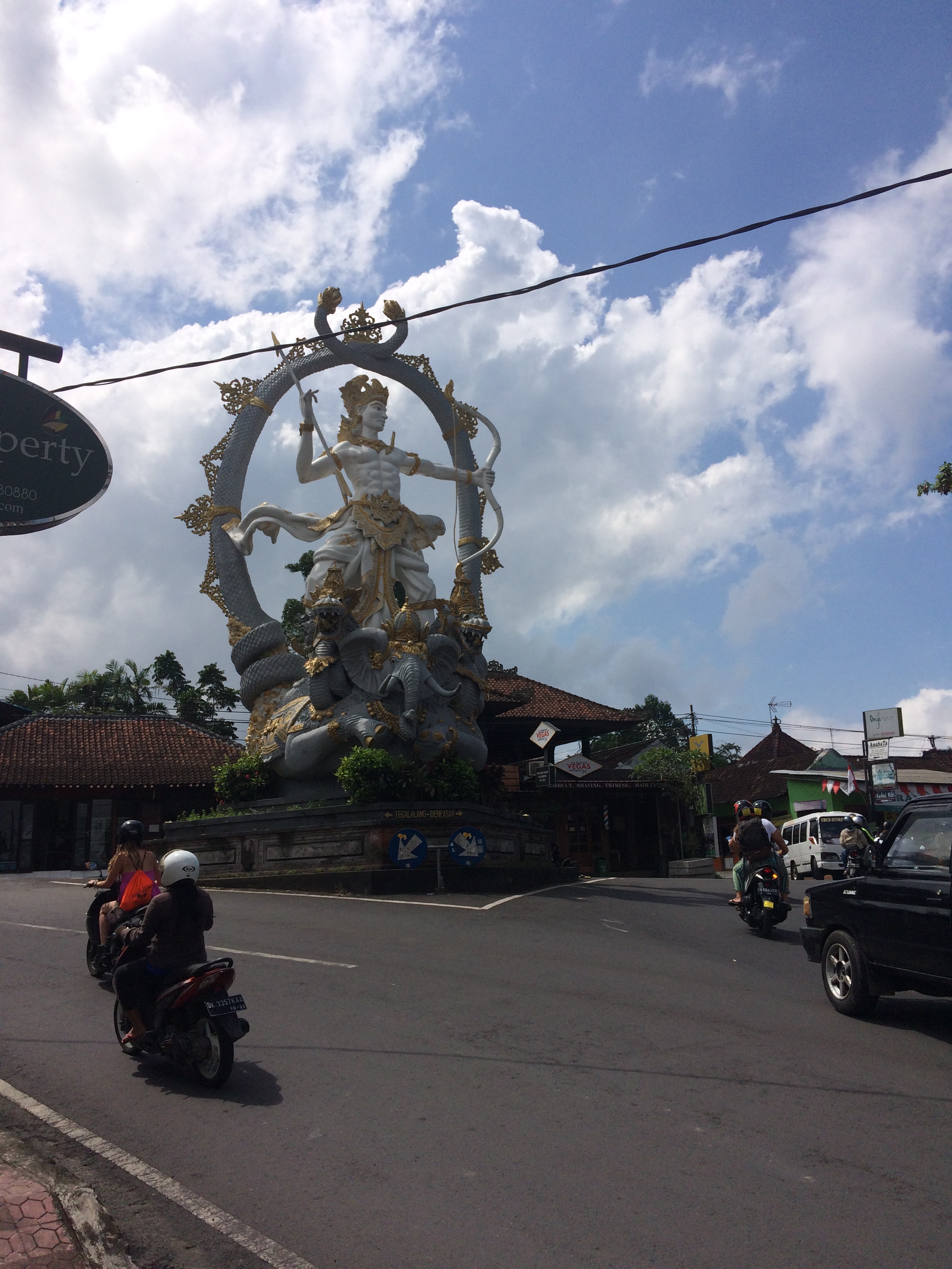 Photo of a giant Hindu statue in the middle of an intersection at the top of the main road in Ubud - the statue is gold and white, a humanoid figure holding a bow and arrow