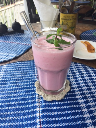A pink milkshake with a sprig of mint on top sits in a glass with a clear plastic straw to drink from it.